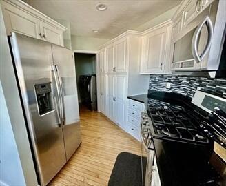 kitchen with appliances with stainless steel finishes, light wood-type flooring, white cabinetry, and decorative backsplash