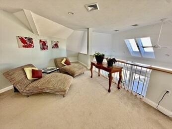 sitting room featuring lofted ceiling with skylight, carpet flooring, visible vents, and baseboards