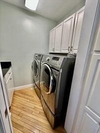 clothes washing area featuring light wood-style flooring, washing machine and dryer, cabinet space, and baseboards