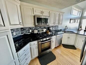 kitchen featuring tasteful backsplash, dark countertops, light wood-style flooring, appliances with stainless steel finishes, and a sink