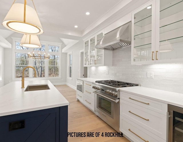 kitchen featuring decorative light fixtures, sink, wall chimney range hood, beverage cooler, and high end stove