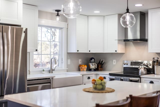 kitchen featuring wall chimney range hood, light countertops, appliances with stainless steel finishes, white cabinets, and a sink