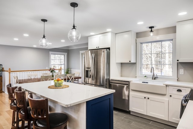 kitchen featuring a kitchen island, a kitchen bar, white cabinets, stainless steel appliances, and a sink