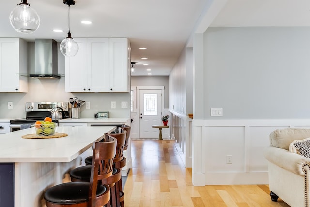 kitchen featuring a wainscoted wall, stainless steel electric stove, light wood-style floors, wall chimney exhaust hood, and light countertops