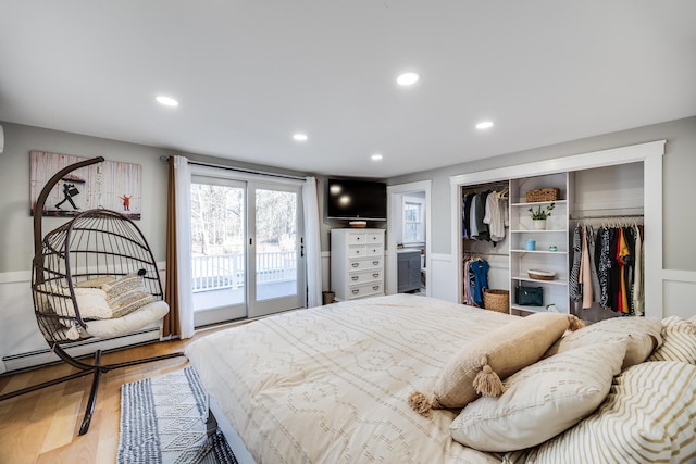 bedroom with a baseboard heating unit, wood finished floors, recessed lighting, a closet, and access to exterior