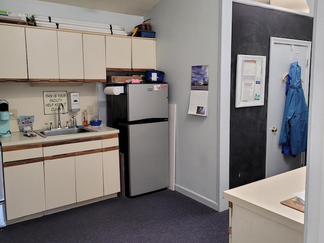kitchen with freestanding refrigerator, dark colored carpet, baseboards, light countertops, and a sink