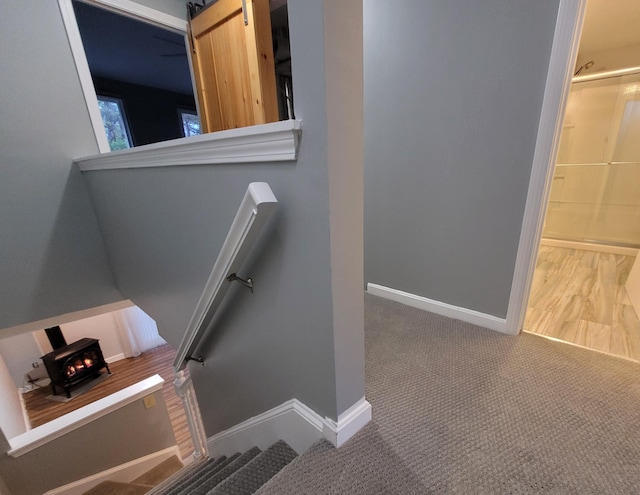 stairway featuring baseboards, a wood stove, and carpet