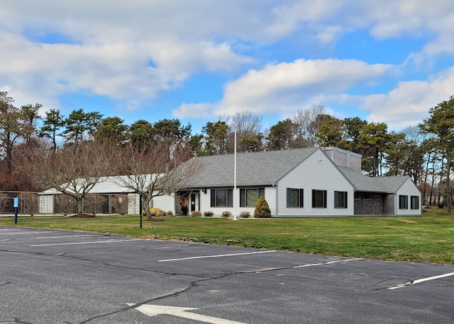 view of front of house featuring roof with shingles, uncovered parking, and a front lawn