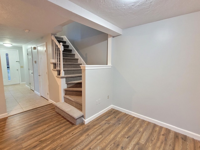stairway featuring baseboards, a textured ceiling, and wood finished floors