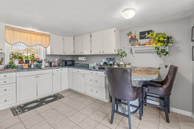 kitchen with black microwave, light tile patterned floors, a sink, white cabinetry, and baseboards