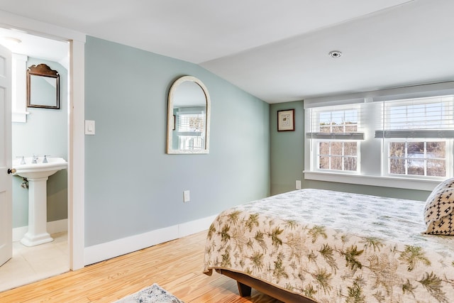 bedroom with hardwood / wood-style floors, lofted ceiling, and ensuite bath