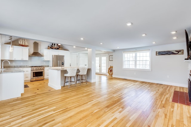 kitchen featuring sink, white cabinets, a kitchen bar, wall chimney range hood, and stainless steel appliances