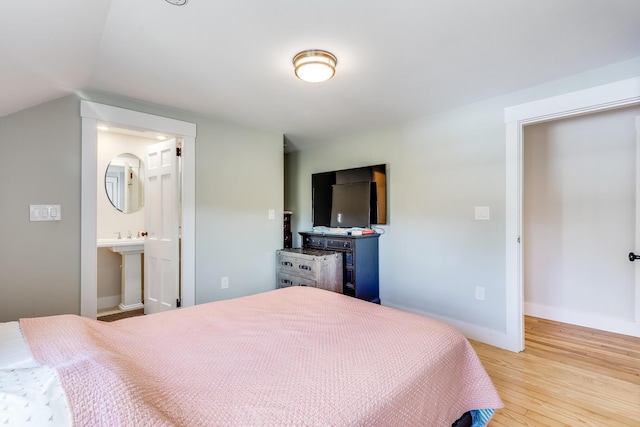 bedroom featuring vaulted ceiling, light hardwood / wood-style flooring, and ensuite bath