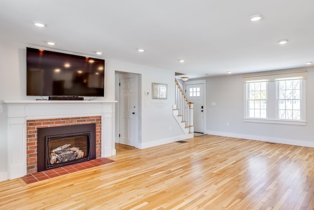 unfurnished living room with a brick fireplace and light hardwood / wood-style flooring