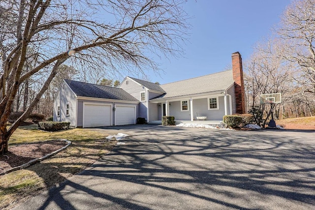 view of front of property featuring a garage, driveway, a porch, and a chimney