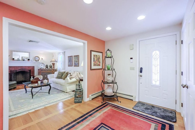 foyer entrance with recessed lighting, a baseboard heating unit, a fireplace, visible vents, and light wood finished floors