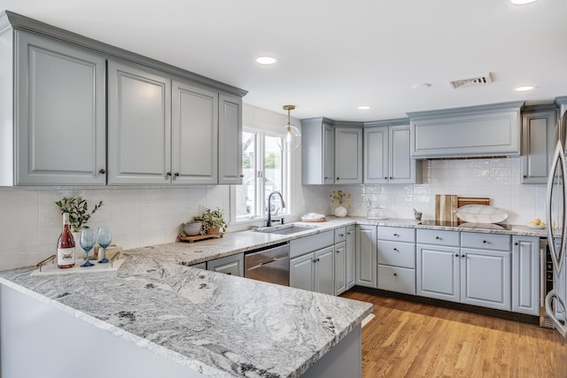 kitchen with a sink, gray cabinetry, stainless steel dishwasher, a peninsula, and tasteful backsplash