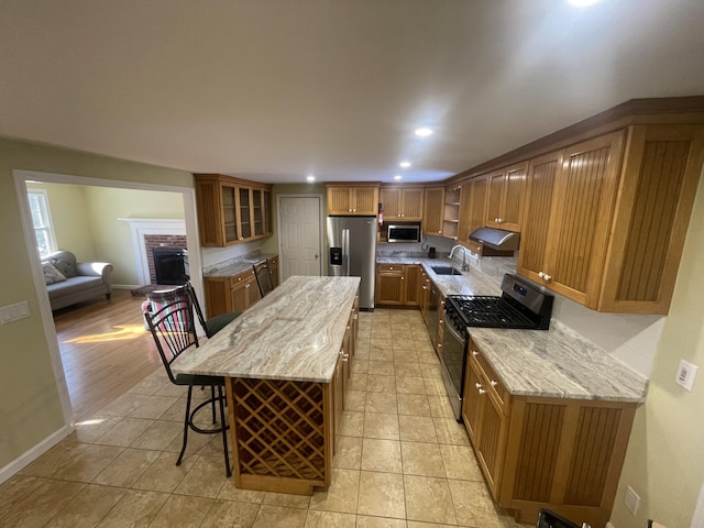 kitchen with a breakfast bar, sink, light stone counters, a center island, and appliances with stainless steel finishes