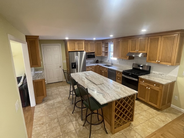 kitchen with sink, a kitchen island, stainless steel appliances, light stone countertops, and a kitchen bar