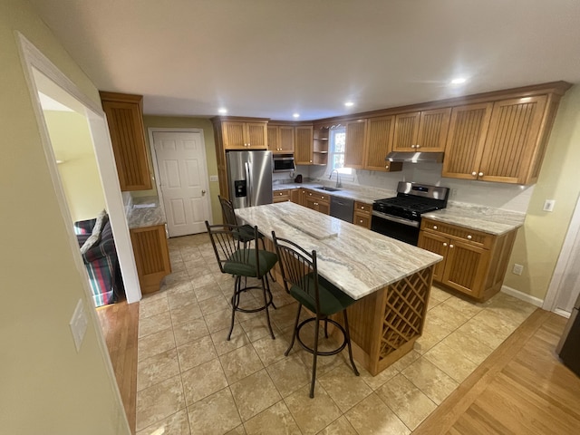 kitchen with sink, a breakfast bar, appliances with stainless steel finishes, light stone counters, and a kitchen island