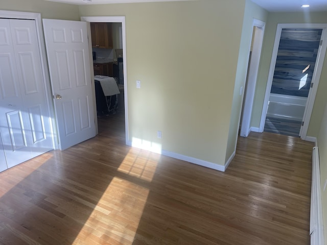 empty room featuring a baseboard heating unit and dark wood-type flooring