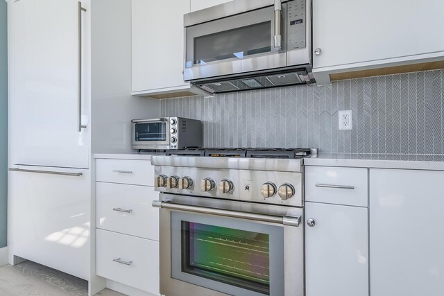 kitchen featuring white cabinetry, light wood-type flooring, high end appliances, and tasteful backsplash