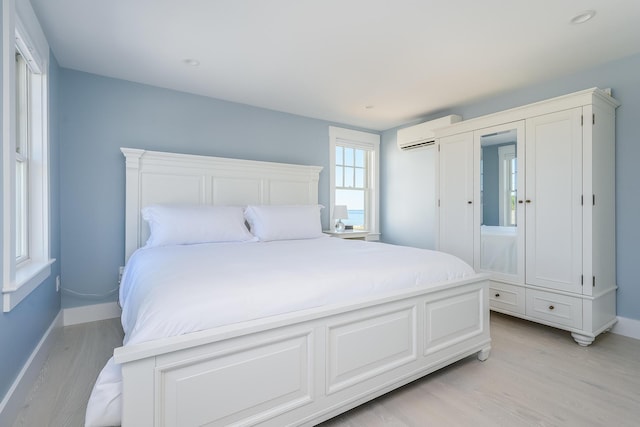 bedroom with light hardwood / wood-style flooring and a wall unit AC