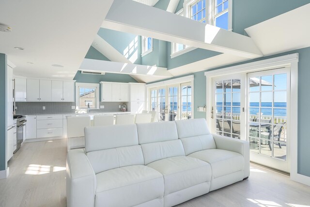 living room with light wood-type flooring, a water view, a high ceiling, and sink