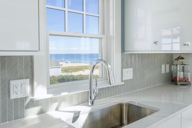 interior details with white cabinets, a water view, light stone countertops, and sink