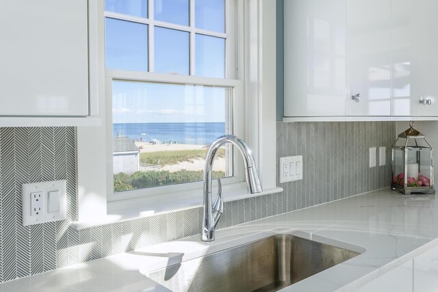 interior details with white cabinets, a water view, light stone countertops, and sink