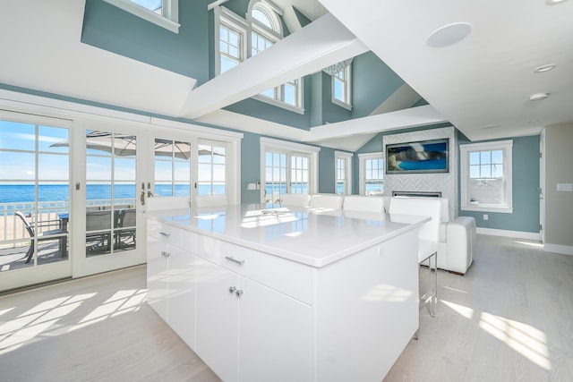 kitchen featuring white cabinets, a kitchen island, a water view, and light wood-type flooring