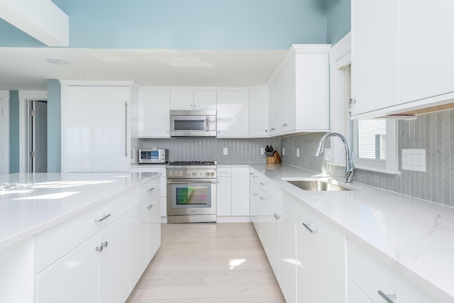 kitchen with sink, backsplash, white cabinets, and appliances with stainless steel finishes