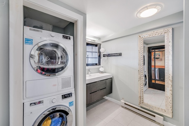 laundry room featuring stacked washer / dryer, baseboard heating, baseboards, and tile patterned flooring