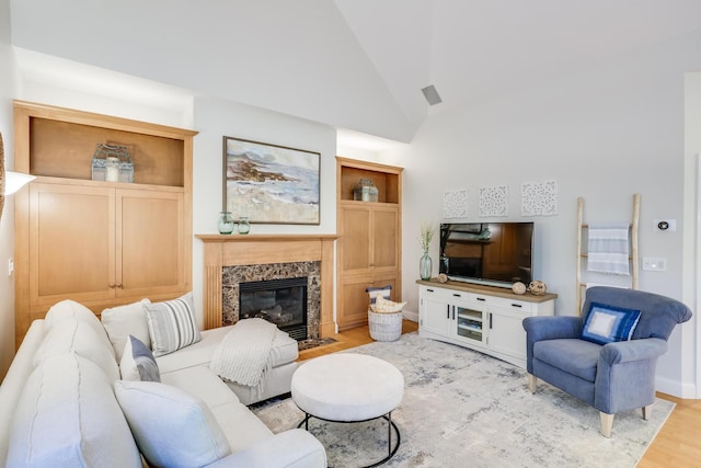 living room featuring high vaulted ceiling, a high end fireplace, and light wood-type flooring