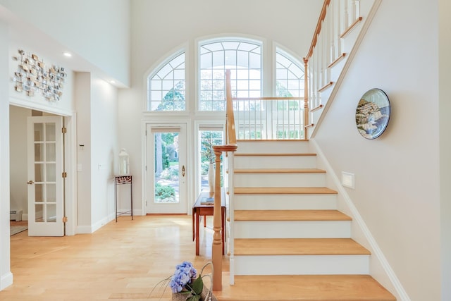 staircase featuring hardwood / wood-style flooring, a baseboard radiator, french doors, and a high ceiling