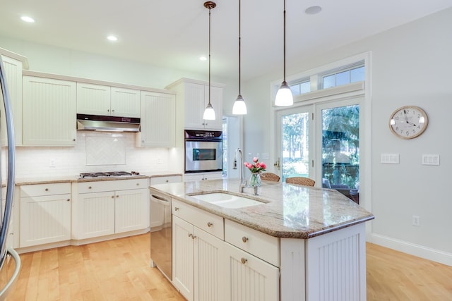 kitchen with sink, light stone counters, hanging light fixtures, stainless steel appliances, and a kitchen island with sink