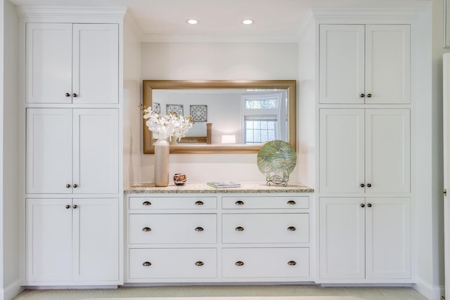 bar featuring light stone counters, ornamental molding, and white cabinets