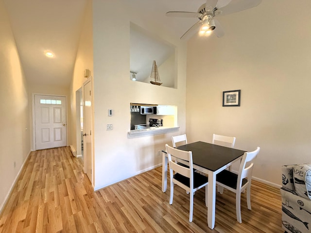 dining room with light wood-type flooring, a ceiling fan, baseboards, and high vaulted ceiling