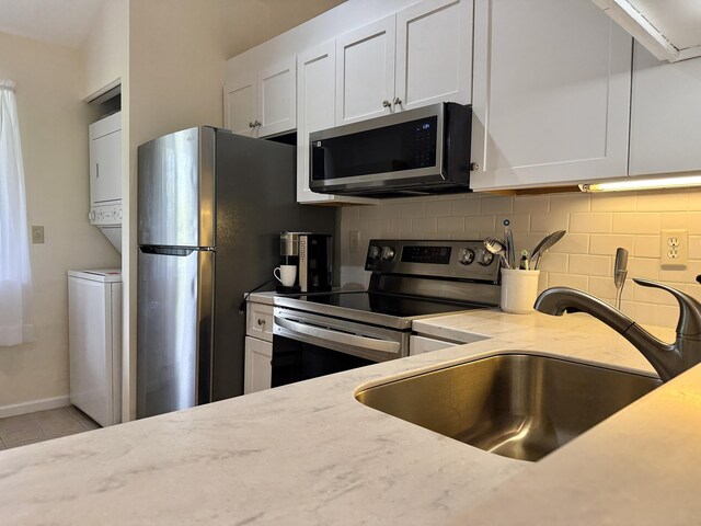 40 Eaton Ln, Brewster, MA 02631 - kitchen with appliances with stainless steel finishes, stacked washer and clothes dryer, backsplash, light tile patterned floors, and white cabinetry