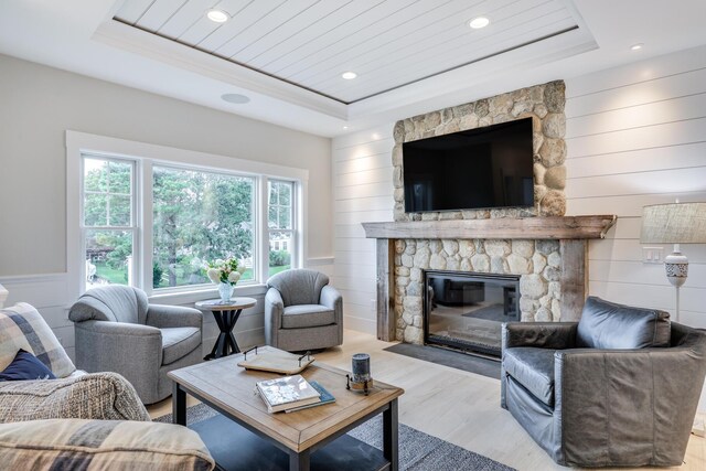 living room with wood walls, light hardwood / wood-style flooring, a fireplace, and a tray ceiling