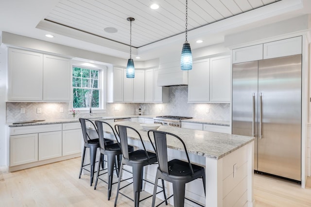 kitchen featuring hanging light fixtures, a raised ceiling, white cabinets, a center island, and stainless steel appliances