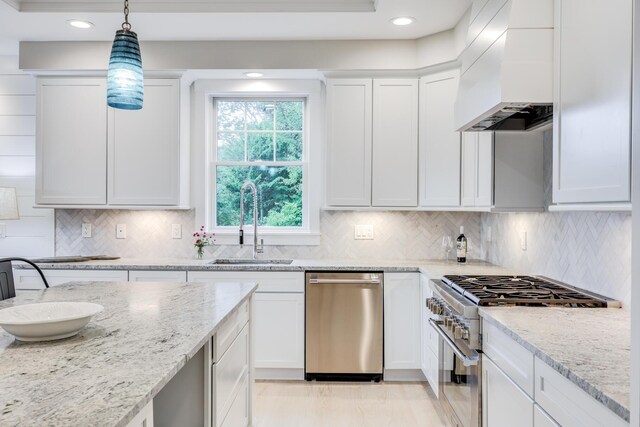 kitchen featuring decorative light fixtures, premium range hood, sink, white cabinets, and stainless steel appliances