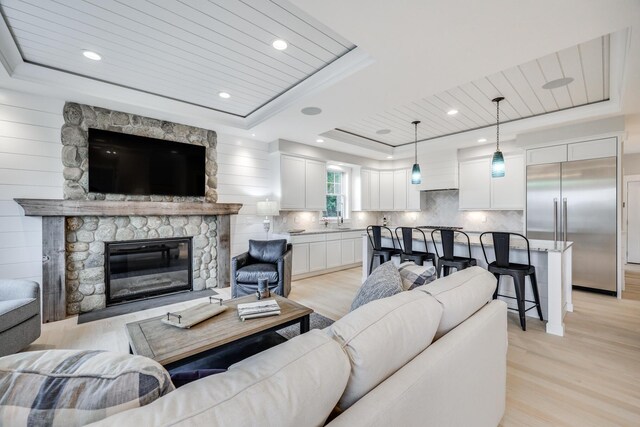 living room featuring light hardwood / wood-style floors, wood ceiling, a stone fireplace, and a raised ceiling