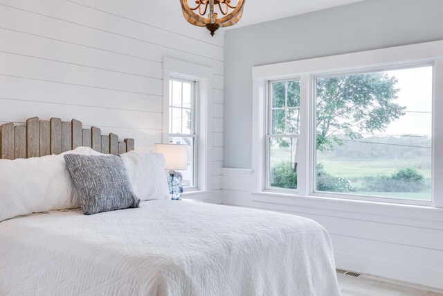 bedroom with wood-type flooring, multiple windows, wooden walls, and a notable chandelier