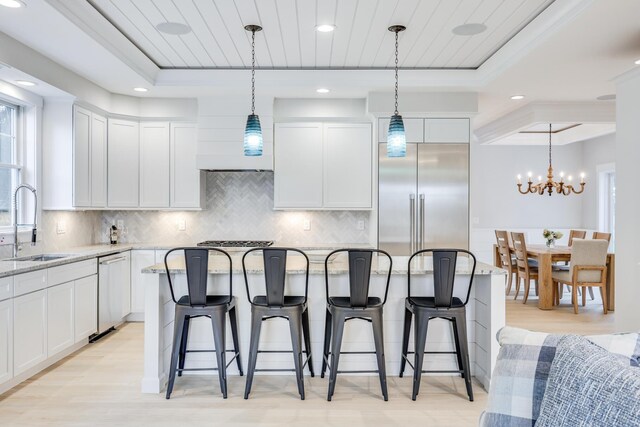 kitchen featuring sink, light stone counters, white cabinets, and pendant lighting