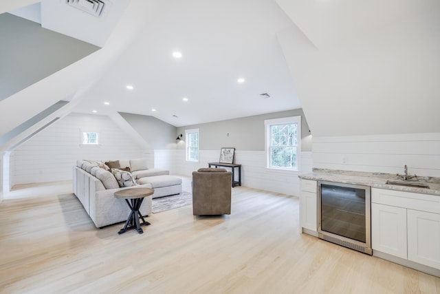 living room with light hardwood / wood-style floors, vaulted ceiling, beverage cooler, and indoor wet bar