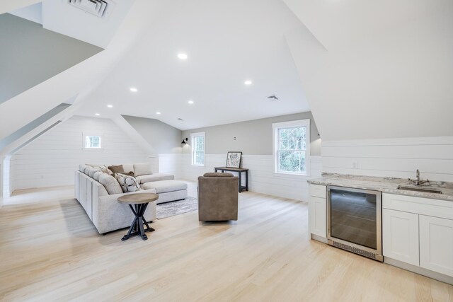 living room with light hardwood / wood-style floors, vaulted ceiling, beverage cooler, and indoor wet bar