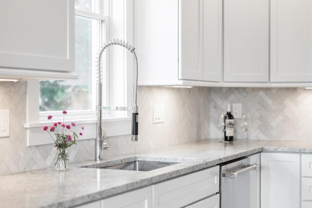 kitchen featuring decorative backsplash, light stone countertops, white cabinets, and sink