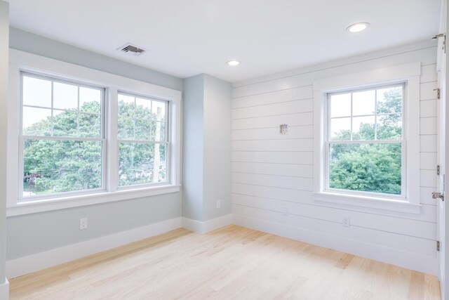 unfurnished room with wood walls, plenty of natural light, and light wood-type flooring