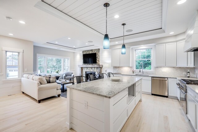 kitchen with hanging light fixtures, appliances with stainless steel finishes, white cabinetry, a tray ceiling, and a center island